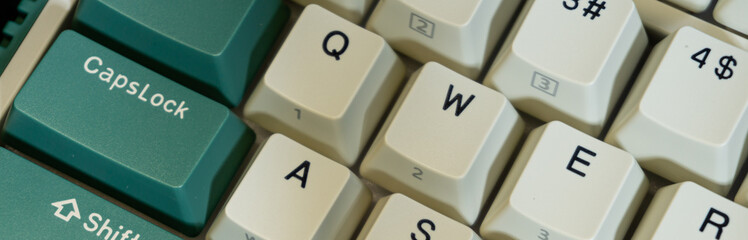Macro view of Caps Lock and QWER keys on a green-and-white mechanical keyboard, crisp focus on front row letters with gentle blur toward the top rows.