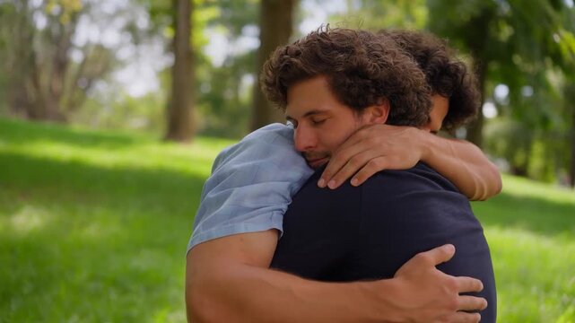 Two friends embracing in a grassy park with trees in the background, symbolizing support, connection, and affection in a natural setting.