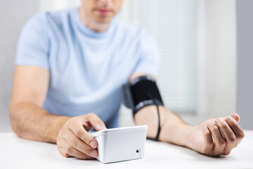 Hands with a tonometer on the table. Man in a shirt measures blood pressure with an electronic tonometer