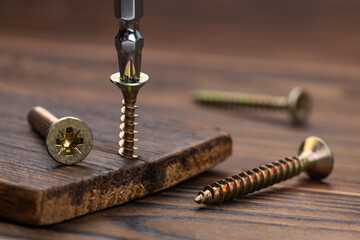 Screwdriver on the screw, screw screwed into timber wood, screw on wooden top table. Close-up, selective focus