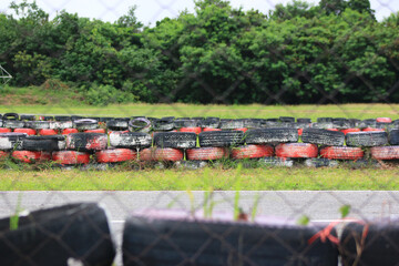 Racing Track Safety Barrier: A row of tires creates a safety barrier, with the greenery and track, ready for race. Capturing strength and environmental preservation.