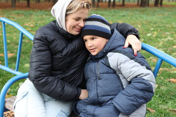 A woman and her son are playing on a playground in an autumn park.