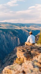 A person sitting on a rocky ledge overlooking a vast canyon during sunset, with serene nature in the background