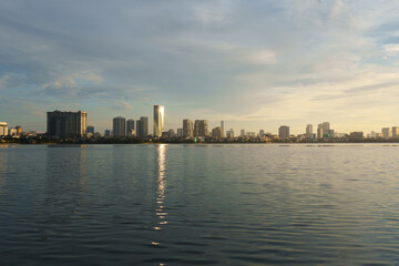 Fototapeta premium Golden hour view of Hanoi skyline from West Lake with sunlight reflecting on the water surface.
