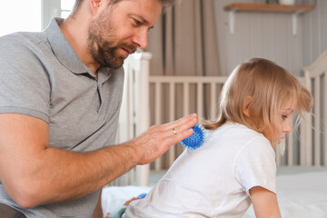 Father using a spiky massage ball for daughter to relieve muscle tension, aid recovery after...