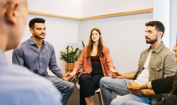 Diverse group of people meditating holding hands in therapy session