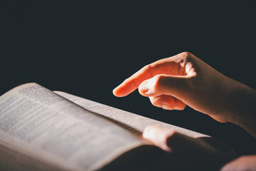 Hands clasped in prayer over the holy Bible, the faithful Christian worships God in church, holding...