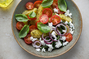 Italian potato salad with cherry tomatoes, green beans, ricotta and basil in a rustic plate, middle close-up, horizontal shot