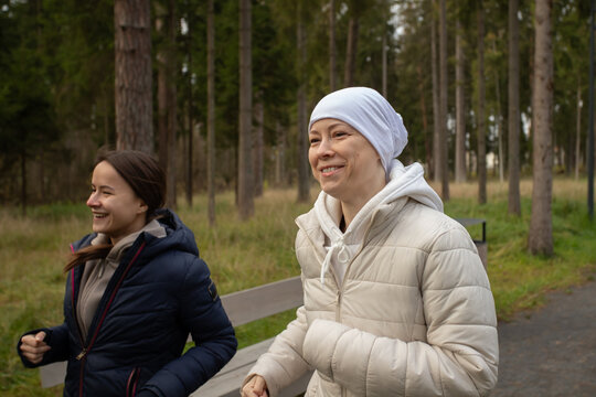 Two women running outdoors in the park, one wearing a headscarf after cancer treatment, both dressed warmly and full of energy