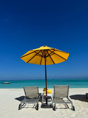 Two chairs beneath umbrella face turquoise sea.