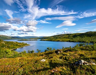 Fototapeta premium Scenic vista of a tranquil lake nestled amidst lush green hills and a bright blue sky