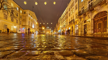 Atmospheric cobblestone street reflecting city lights in an old European city at night.
