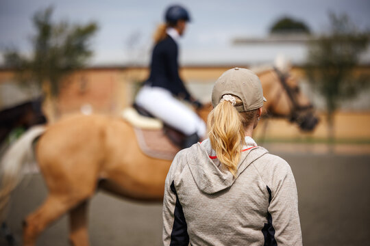 Horse trainer closely monitoring rider preparing for dressage event. Horseback riding in equestrian paddock - Powered by Adobe