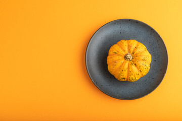 Orange Pumpkin on blue plate on orange pastel paper. Top view, copy space