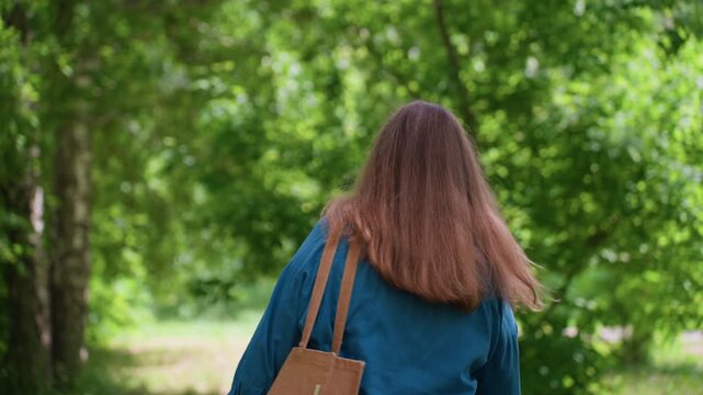 Elegant lady wearing sunglasses and casual outfit turns around in green park surrounded by trees and sunlight, preparing to walk away with calm confident expression under warm summer light breeze