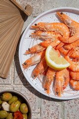 Top view of cooked shrimps on plate and Spanish tapas and elements under hard sunlight