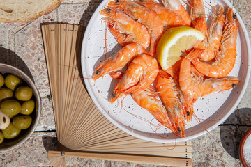 Top view of cooked shrimps on plate and Spanish tapas and elements under hard sunlight