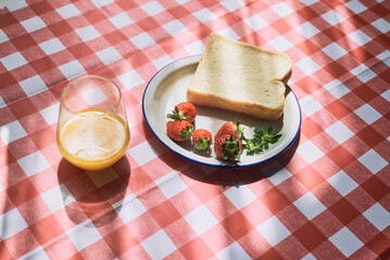 Simple breakfast with toast, strawberries, and orange juice on checkered tablecloth