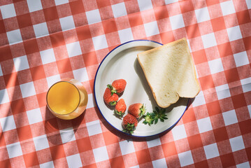 Simple breakfast with toast, strawberries, and orange juice on checkered tablecloth