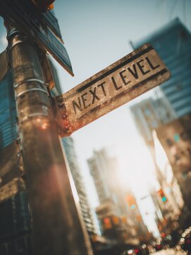 Close-up of a weathered street sign reading Next Level against a cityscape backdrop during sunset