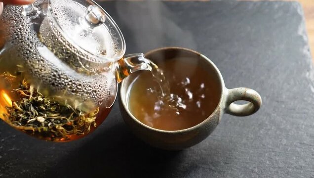 Tea Ceremony: A moment of peace unfolds as the steaming tea, poured from a transparent glass teapot into a rustic ceramic cup, ready for the upcoming enjoyment and flavor. 