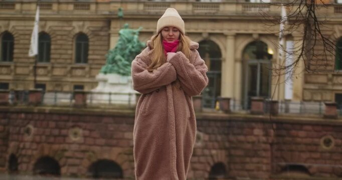 Germany - 26.12.2022: young European Ukrainian woman walks in autumn winter in an empty park, observing nature. warm autumn winter clothes, faux fur coat, Eco fur, knitted hat, scarf, gloves. girl