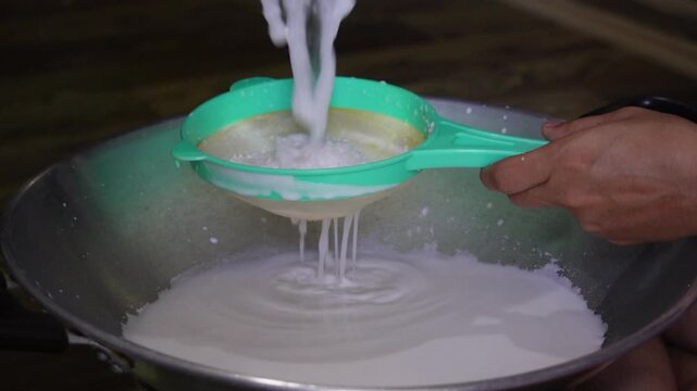 Close-up of coconut milk being strained through a sieve into a bowl.
