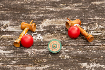 Two Japanese cup-and-ball toys (kendama) and a spinning top (koma), displayed on a weathered rustic wooden table. Symbolizes traditional Japanese games, culture, and nostalgia.