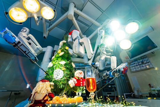 Christmas decorations with surgical robot and champagne glass. Festive setup with Christmas tree, champagne glass, and surgical robot arms in illuminated operating room.