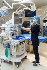 Nurse adjusting equipment monitor in hospital operating room. Medical nurse wearing mask and gloves...