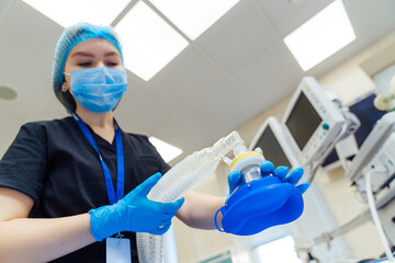 Nurse holding anesthesia breathing mask in surgery room. Female nurse with blue gloves and mask holding anesthesia breathing mask in modern surgery room.