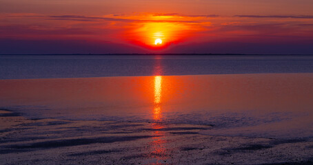 Romantic and very colorful sunset panorama over the North German Wadden Sea National Park at low tide near the East frisian island of Wangerooge. Nature reserve and popular World Heritage Site. 