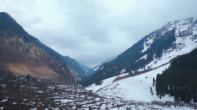 Wide angle shot of snowy Himalayan mountain range with dark clouds above it during the winter season as seen at Betaab Valley in Pahalgam, Jammu and Kashmir, India. Scenic snowy Himalayas in winter. 