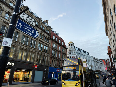 Bustling Manchester Oldham street scene with historic buildings, a yellow bus, and shoppers in the city UK
