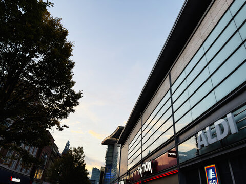 Evening in Manchester city street with ALDI store and modern glass building facade