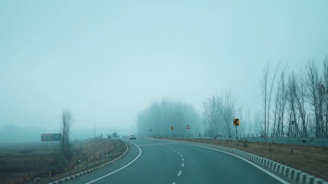 4K shot of foggy road with bare trees and dry grass on both sides, creating mysterious and calm atmosphere. Road covered in thick fog during winter morning in Kashmir, India. Travel, Road trip concept