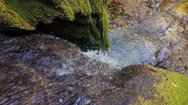 Small waterfall pouring between moss-covered rocks in mountain creek, slow motion capture emphasizing clarity and freshness