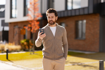 Man walking outdoors holding smartphone checking messages