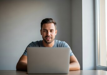 Relaxed young man using laptop by window in minimal home workspace
