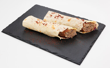 Two crispy rolled Kebabs filled with seasoned beef rest on a dark slate board, lightly dusted with red chili powder