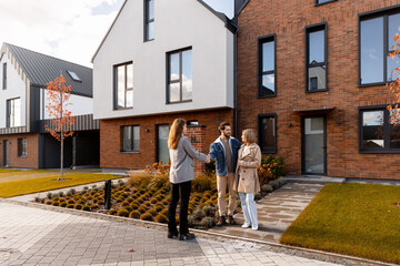 Real estate agent shaking hands with happy couple buying house