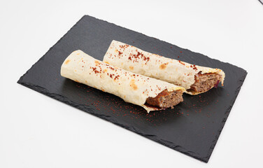 Two crispy rolled Kebabs filled with seasoned beef rest on a dark slate board, lightly dusted with red chili powder
