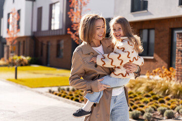 Mother carrying daughter smiling during autumn walk outdoors