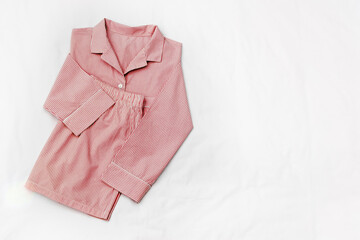 Top view of folded red striped pajama set on white bed. Minimal style, cozy, comfort pyjamas. Pink Sleepwear fashion concepts, wellness, calm lifestyle, home aesthetics, morning routines