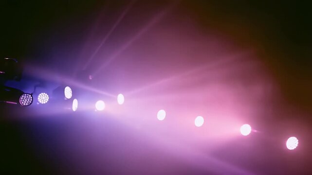 A captivating wide shot features a dynamic array of stage lights creating an immersive and vibrant atmosphere. Multiple spotlights emit powerful, sweeping beams of white, purple, and pink light throug