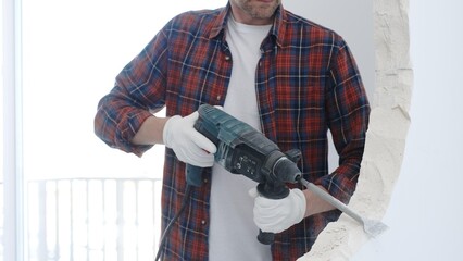 Male construction worker wearing red checkered shirt and protective white gloves is demolishing...