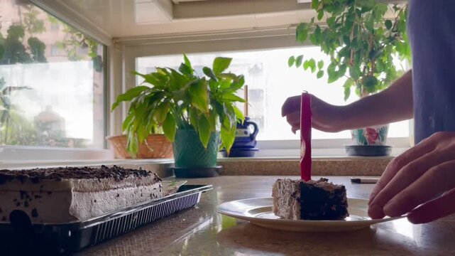 Servir en plato trozo de tarta de cumplea&ntilde;os con vela roja y mano encendiendo con mechero