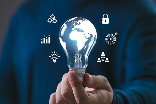 Hand holding a glowing light bulb with world map and business icons representing global innovation, creative idea, technology development, and strategic business growth for the modern world.