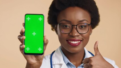 Smiling African American Female Doctor Holding Smartphone with Green Screen and Giving Thumbs Up Promoting Medical App or Telemedicine Service.