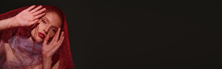 Elegant young woman in red veil showcasing beauty and fashion in a studio setting